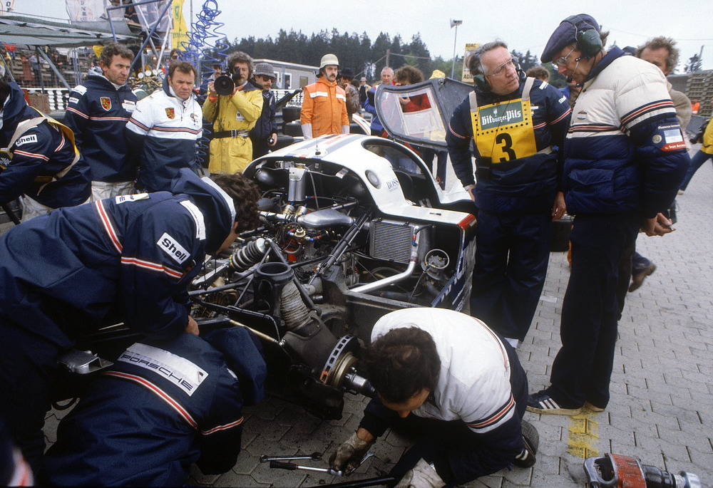 956 KH during the pit stop at the Nürburgring (1000 km) in 1983. From right to left: Peter Falk, Helmuth Bott, behind them (half covered) Jochen Mass. To the left of the car (with blue/white jacket) Valentin Schäffer, next to him on the left is Ludwig Lehner. 956-KH-during-the-pit-stop-at-the-Nürburgring-1000-km-in-1983.